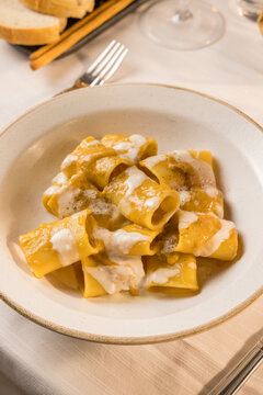 Gourmet presentation of traditional Italian paccheri pasta coated in a rich, creamy cheese sauce. The image highlights the large, tube-shaped pasta perfectly cooked and smothered in a velvety melted c