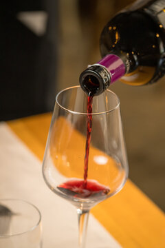 Sophisticated image capturing red wine being elegantly poured from a bottle into a clear glass by a server in a fine dining restaurant, set against a blurred background of a busy, atmospheric dining r