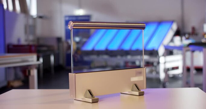 A modern transparent glass railing prototype with a metal handrail standing on a wooden table in a workshop