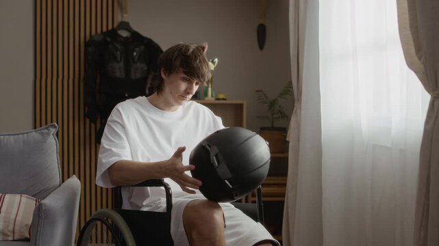 Medium shot of upset man in wheelchair taking off moto helmet and starting looking at it, remembering moto experience