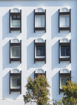 Aerial view of the facade of a white building featuring a grid of nine windows with dark frames and arched decorative tops under bright sunlight in Taiwan.