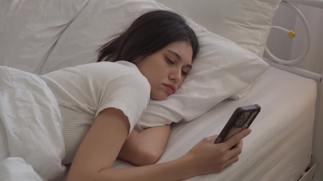 woman having sore and tired eyes when using smartphone while lying in bed at night. Young woman cannot sleep from insomnia
