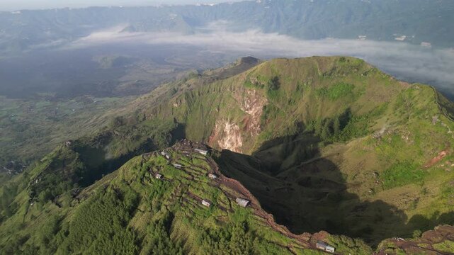 Aerial view of The peak of Mount Batur in Kintamani, Bali, Indonesia, showing its active crater with smoke rising in the morning light.