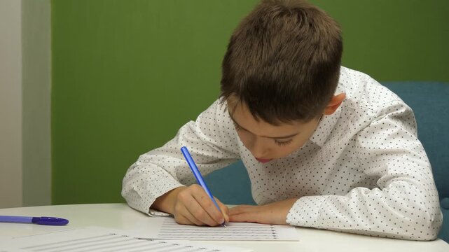 Child boy writing music homework at table, focused boy studying notes on paper. Concept of education, concentration and learning at home, cozy indoor environment. Kid focuses on homework task at home.