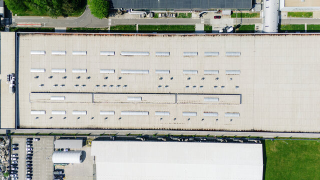 Aerial view of a large industrial warehouse roof with rows of skylights, ventilation systems, and an adjacent parking lot Sremska Mitrovica, Vojvodina, Serbia.