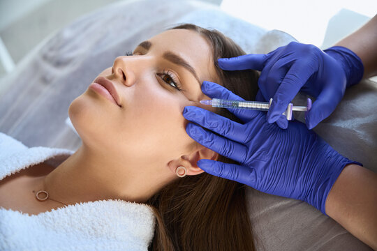 Close up beautician wearing hygiene gloves injecting filler for facial treatment to female