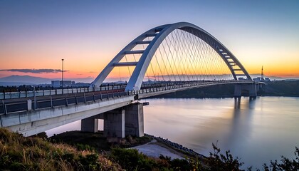 Obraz premium A large arched bridge spans a body of water at sunset