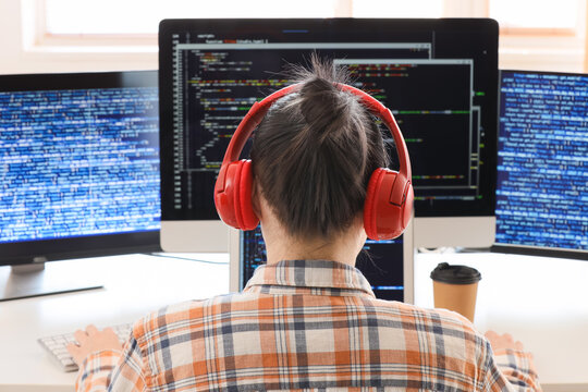 Female programmer with headphones working at desk in office, back view