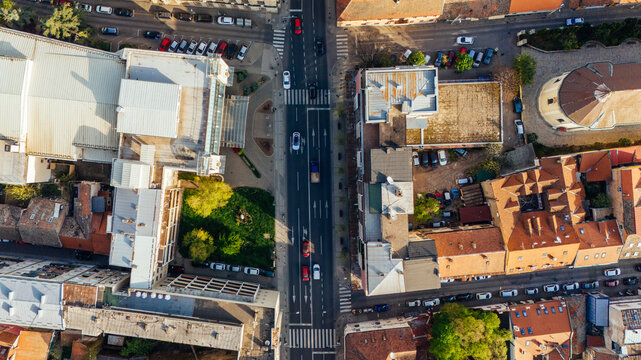 Aerial view of the historic Zemun district featuring red-tiled rooftops, urban streets with moving cars, and lush green trees under bright sunlight in Belgrade, City of Belgrade, Serbia.
