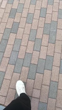 POV of white sneakers walking on brick pavement, vertical video