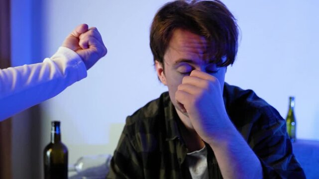 Close-up of a depressed drunk man whose glass of alcohol is taken away by someone's hand, who then shakes a fist at him. Concept of alcoholism, addiction, family conflict, and intervention.4k footage