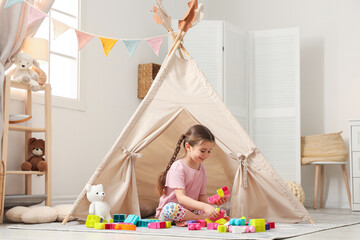 Little girl playing with building blocks near toy wigwam in playroom © New Africa