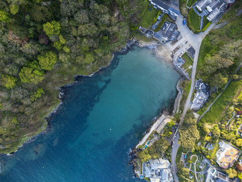 Aerial view of the turquoise waters of the secluded Readymoney cove in Fowey surrounded by lush green woodland and coastal houses in Fowey, England, United Kingdom.