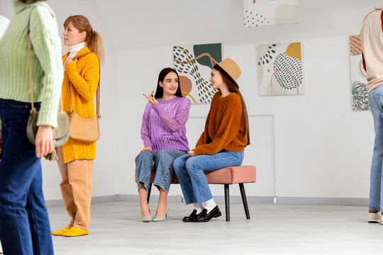 Young women sitting on bench at exhibition in art gallery