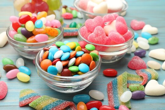 Delicious colorful candies in glass bowls on blue wooden table, closeup