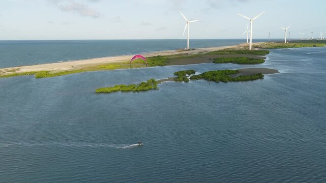 Kitesurfer rides shallow lagoon near Ilha do Guajiru S&atilde;o Gon&ccedil;alo do Amarante Cear&aacute; Brazil with onshore wind turbines of Ta&iacute;ba complex and Atlantic coastline, drone tracking shot