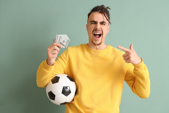 Happy young man with soccer ball pointing at money on green background. Sports bet concept