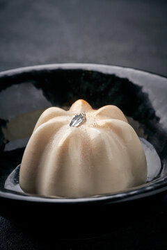 Elegant panna cotta or mousse dessert decorated with silver leaf in a black bowl. Minimalist gourmet pastry on dark background
