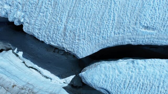 Top-down aerial panning shot over a deep crevasse and icy fissures in a glacier within the Chamonix Alps. Ideal for nature, environment, and climate change content