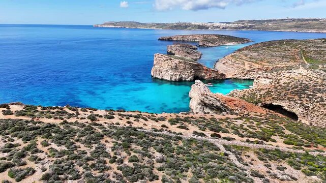 Blue Lagoon in Comino Għajnsielem Gozo Region Malta with carbonate platform and submerged limestone shelf creating turquoise basin between Comino and Cominotto high water clarity drone pull away
