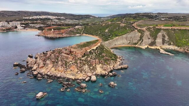Aerial drone view of Qarraba Bay in Malta with steep limestone cliffs, rocky coastline, and clear turquoise water forming small coves along the rugged shore in daylight.