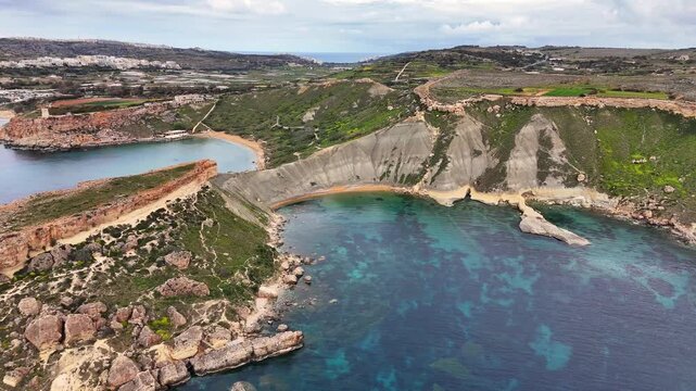 Drone aerial of Qarraba Bay in Malta showing steep limestone cliffs, rocky shoreline, and small turquoise coves along clear calm sea under soft daylight.