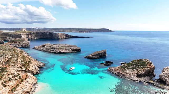 Aerial view of Blue Lagoon in Comino, Malta, showing turquoise water, rocky coastline and small boat anchored in a calm bay under daylight.