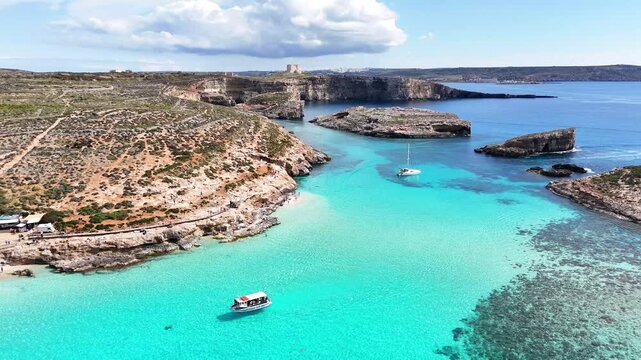 Aerial view of Blue Lagoon in Comino, Malta, with turquoise water, rocky coastline, small anchored boats and a wide coastal bay in daylight.