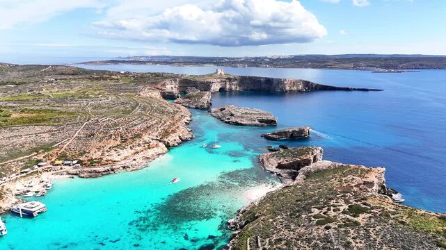Blue Lagoon in Comino Għajnsielem Gozo Malta with limestone headlands and shallow turquoise basin over carbonate seabed between Comino and Cominotto islands, clear Mediterranean drone forward flyover