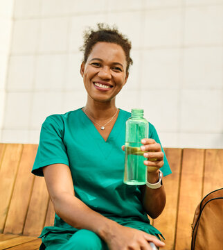 Young woman or a nurse or a doctor during office hours break enjoying a fresh salad and drinking water in a park during a sunny day while smiling and relaxing on a bench