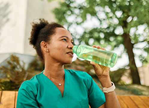 Young woman or a nurse or a doctor during office hours break enjoying a fresh salad and drinking water in a park during a sunny day while smiling and relaxing on a bench