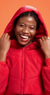 Black woman, face and happy with hoodie in studio for fashion, pride or excited by orange background. Gen z girl, person and portrait with smile, winter outfit and laugh with trendy style in Nigeria