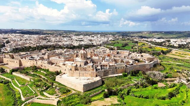 Mdina in Northern Region Malta showing limestone bastioned walls with St Paul Cathedral and Rabat surroundings with visible road network agricultural landscape, orbiting establishing shot
