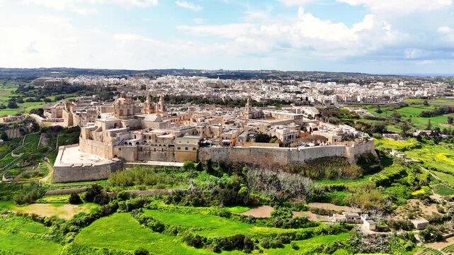 Mdina Northern Region Malta seen from north with St Paul Cathedral rising above fortified walls overlooking Rabat and surrounding terraced fields with dry farming agriculture, drone clockwise orbit