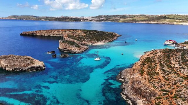 Drone aerial over Blue Lagoon in Comino, Malta showing rocky coastline and vivid turquoise water, with layered cliffs and calm sea under clear sunny light.