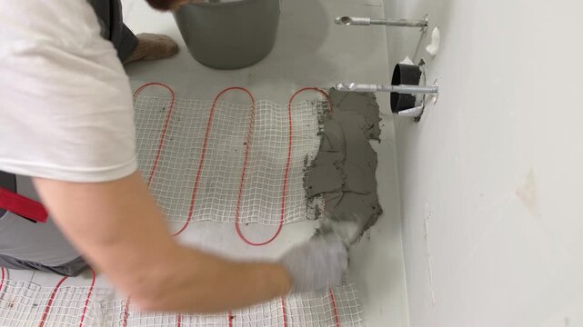 Electric Heating Mat Installing in the Tile Adhesive. Underfloor Dual Core Fiberglass Mesh Mat. Warm Floor Heating System. Warming. Worker Applying Concrete Mortar for Warm Floor. Renovation work. 4K