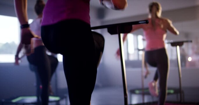 Woman in pink top and black leggings performing leg lifts on mini trampoline in studio