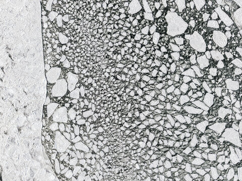 Aerial view of fragmented white ice floes scattered across dark, frigid waters, contrasting sharply with a solid icy expanse to the left, Hono, Vastra Gotaland County, Sweden.