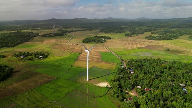 Aerial flyover of wind turbines rising above patchwork farmland and dense forest landscape in Guimaras Island, Visayas, Philippines