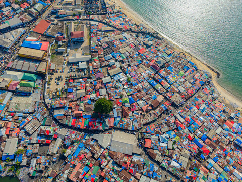 Aerial view of vibrant rooftops cascade towards the shoreline, contrasting with the tranquil turquoise ocean, a bustling tapestry of life unfolds, Monrovia, Liberia.