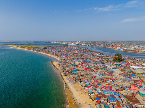 Aerial view of a sprawling settlement, where vibrant rooftops meet the tranquil ocean, divided by a thin strip of sandy beach, Monrovia, Liberia.