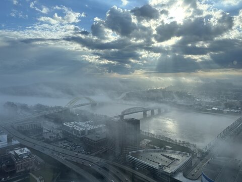 Aerial view of ethereal fog blanketing the Ohio River and its bridges, with dramatic sunbeams piercing through the clouds over Cincinnati, Ohio, United States.