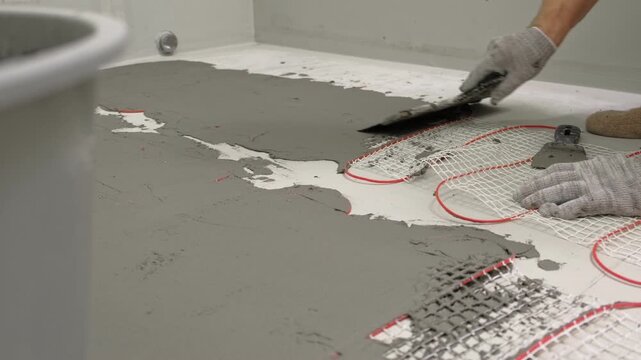 Electric Heating Mat Installing in the Tile Adhesive. Underfloor Dual Core Fiberglass Mesh Mat. Warm Floor Heating System. Warming. Worker Applying Concrete Mortar for Warm Floor. Renovation work. 4K