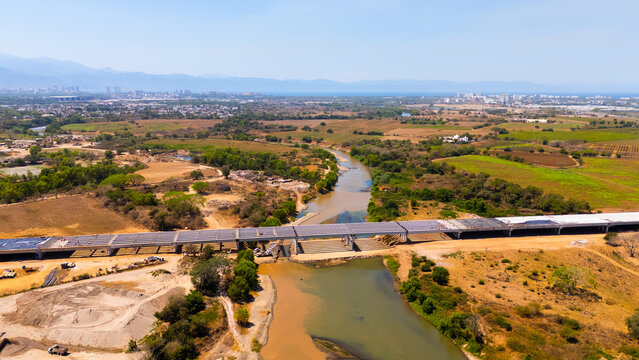 Aerial view of a muddy river and arid plains bisected by a new bridge under construction, leading to a distant city, Puerto Vallarta, Jalisco, Mexico.
