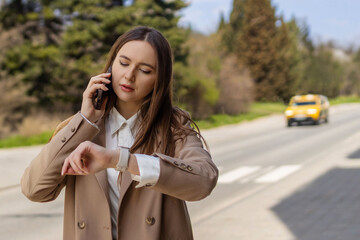 Young woman talking on smartphone and checking time while waiting for taxi on city street, urban lifestyle and transportation concept © руслан малыш