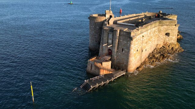 Aerial view of Chateau du Taureau, a formidable stone fortress with rugged, sun-kissed walls emerging from the deep blue, calm sea, Plouezoc'h, Bretagne, France.