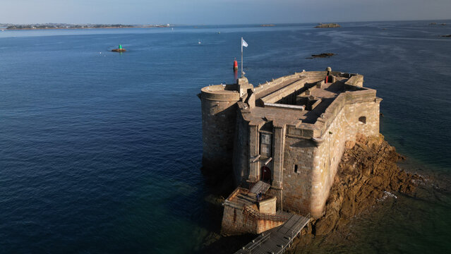 Aerial view of Chateau du Taureau, a stone fortress with a flag, rises majestically from the sea, its ancient walls echoing tales of maritime history, Plouezoc'h, Bretagne, France.
