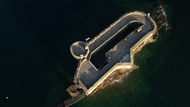 Aerial view of the imposing Chateau du Taureau, a stone fortress rising from the dark waters, its weathered walls catching the golden light, Plouezoc'h, Bretagne, France.