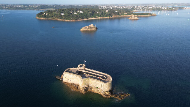 Aerial view of the historic Chateau du Taureau fortress, a rugged stone sentinel in the deep blue sea, contrasting with distant green islands, Plouezoc'h, Bretagne, France.