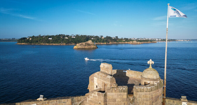 Aerial view of Chateau du Taureau's rugged stone, the deep blue sea, and a verdant island under a brilliant sky, Plouezoc'h, Bretagne, France.